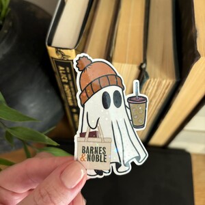 May include: A white ghost wearing an orange and brown beanie hat, holding a brown bag with the text "Barnes & Noble" and a cup of iced coffee.
