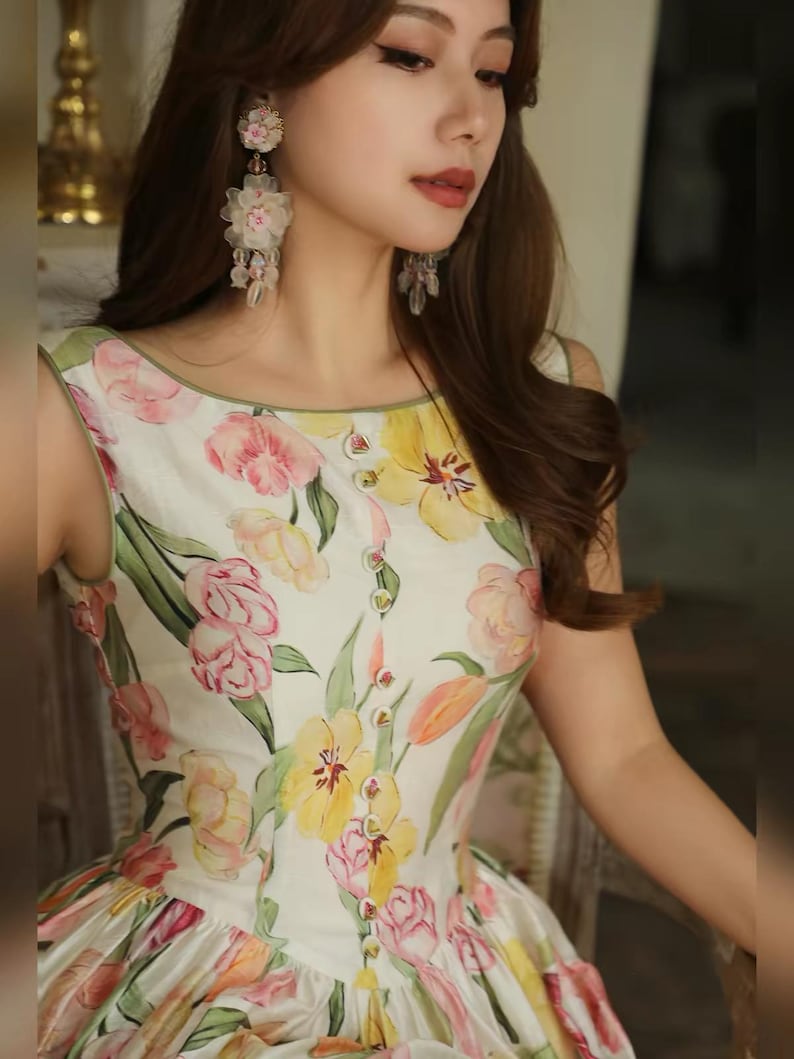 May include: A sleeveless white dress adorned with a floral print featuring pink, yellow, and orange blooms. The dress has a round neckline and small buttons. A light, summery dress, perfect for warmer weather.