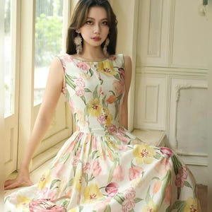 May include: A sleeveless floral dress with a white base, adorned with yellow, pink, and green tulip patterns. The dress has a fitted bodice with small buttons and a flared skirt. Ideal for warmer weather, the dress is suitable for spring or summer.