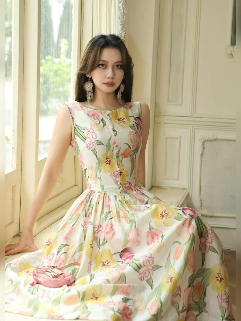 May include: A sleeveless floral dress with a white base, adorned with yellow, pink, and green tulip patterns. The dress has a fitted bodice with small buttons and a flared skirt. Ideal for warmer weather, the dress is suitable for spring or summer.