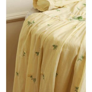 Puede incluir: Tela amarillo p&aacute;lido con dise&ntilde;os florales bordados en verde y amarillo. La tela est&aacute; fruncida y drapeada, con la palabra "FABRIC" en la parte superior. El bordado es detallado y la tela parece ligera.