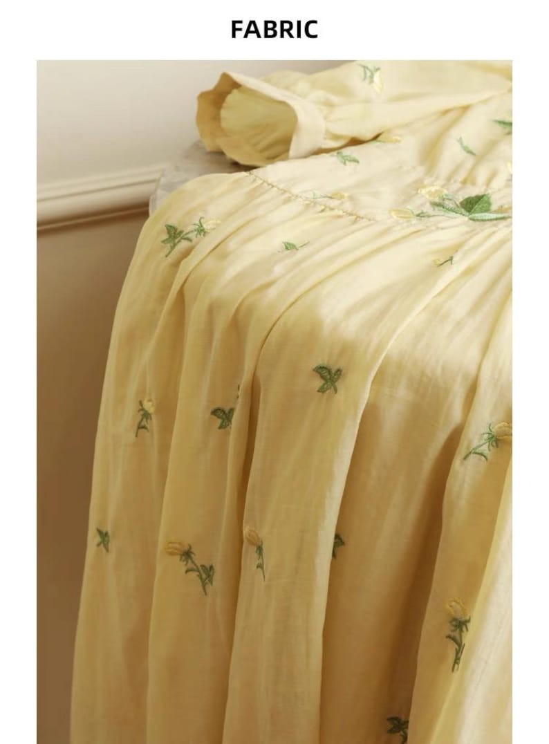 Puede incluir: Tela amarillo p&aacute;lido con dise&ntilde;os florales bordados en verde y amarillo. La tela est&aacute; fruncida y drapeada, con la palabra "FABRIC" en la parte superior. El bordado es detallado y la tela parece ligera.