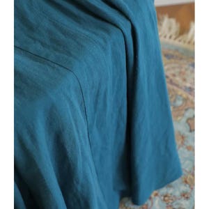 May include: Close-up of a teal-colored fabric with visible texture and folds. The fabric appears to be a flowing material, possibly linen or a similar lightweight textile. The image highlights the color and drape of the fabric.