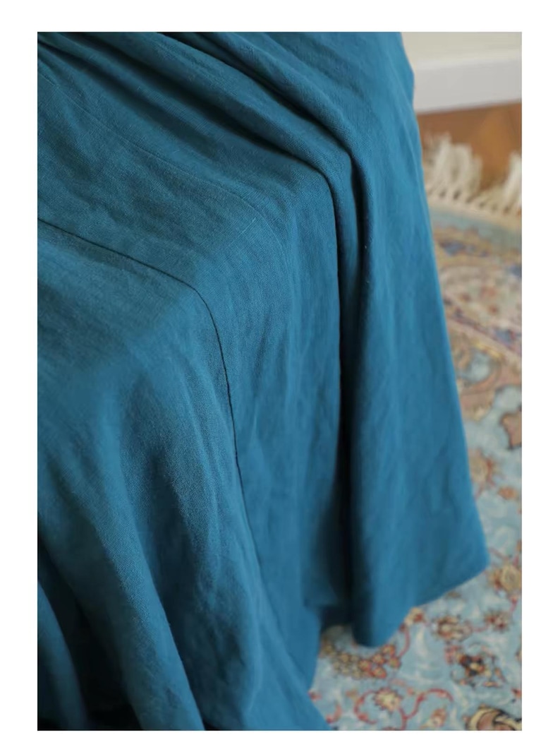 May include: Close-up of a teal-colored fabric with visible texture and folds. The fabric appears to be a flowing material, possibly linen or a similar lightweight textile. The image highlights the color and drape of the fabric.