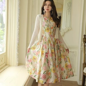 May include: A floral print dress with a white cardigan. The dress features a pattern of pink, yellow, and orange flowers on a cream background. The cardigan is a light, open-front style. The person is wearing gold sandals.