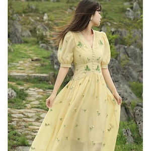 Puede incluir: Vestido amarillo claro con escote en V y mangas cortas abullonadas. Cuenta con detalles florales verdes bordados y peque&ntilde;os botones. La falda fluida est&aacute; decorada con bordados florales dispersos. El vestido es de largo midi.