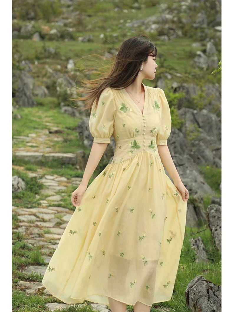 Puede incluir: Vestido amarillo claro con escote en V y mangas cortas abullonadas. Cuenta con detalles florales verdes bordados y peque&ntilde;os botones. La falda fluida est&aacute; decorada con bordados florales dispersos. El vestido es de largo midi.