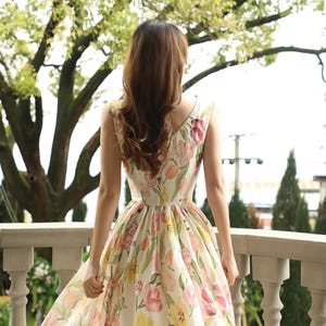May include: A floral print dress with a V-neck. The dress has a pattern of pink, yellow, and green flowers on a white background. The dress is sleeveless and appears to be made of a lightweight fabric. The dress is suitable for warm weather.