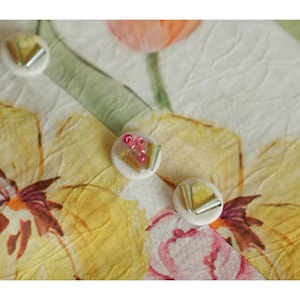 May include: Close-up of a floral pattern with three decorative buttons. The background features yellow, pink, and white flowers with green leaves. The buttons are white with silver and pink accents, adding a touch of elegance to the design.