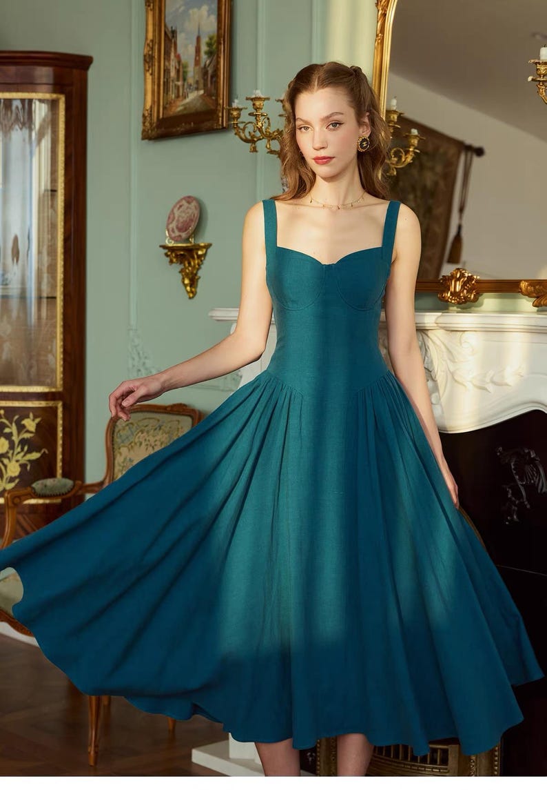 May include: A teal-colored dress with a sweetheart neckline and wide straps. The dress features a fitted bodice and a full, pleated skirt. The fabric appears to be a textured linen or similar material. The dress is a vintage or retro style.