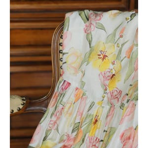 May include: White fabric featuring a watercolour floral design of yellow, pink, and orange tulips and green leaves. The fabric is draped over a wooden chair. The word "FABRIC" is at the top.