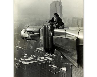 May include: A black and white photograph of a woman sitting on a gargoyle on top of a building in New York City. The woman is looking down at the city below. The gargoyle is a large, ornate sculpture of a bird.