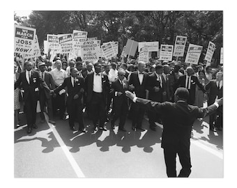 May include: Black and white photograph of a large group of people marching in a street. The people are holding signs that read "We March for Jobs", "We Demand Voting Rights Now", "End Segregated Rules in Public Schools", and "We Demand Equal Rights Now".