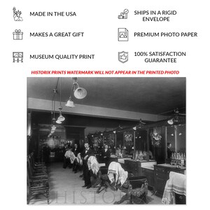 May include: Black and white photograph of a barbershop interior. The barbershop has multiple barber chairs, mirrors, and a counter with bottles of hair products. The photo was taken in the early 1900s.