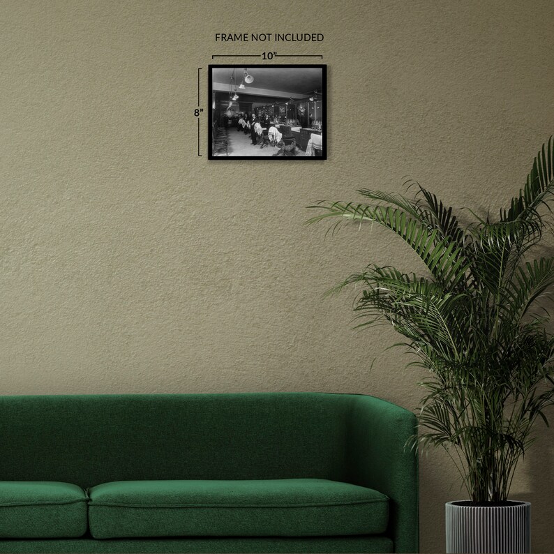 May include: Black and white photograph of a barbershop interior with customers getting haircuts. The photo is framed in a black frame and measures 8 inches by 10 inches.