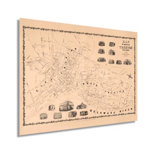 May include: A vintage map of the city of Trenton, New Jersey, printed in black and white on a cream-colored background. The map shows the streets and buildings of the city, including the Delaware River.