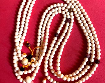 May include: A white beaded mala necklace with a tassel and colorful beads. The mala is laid out on a red surface.