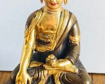 May include: A gold-painted bronze statue of Buddha sitting in meditation with a lotus flower in his lap. The statue is on a base with a decorative border.