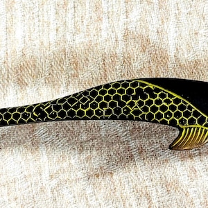 May include: A black and gold door handle shaped like a stylized fish with a honeycomb pattern. The handle is made of metal and has a traditional design.