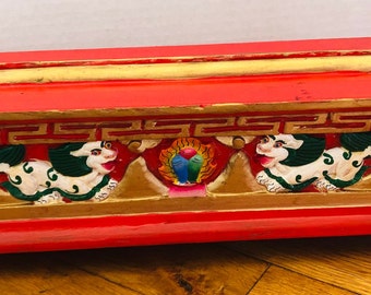 Peut inclure: Un brûle-encens en bois rouge avec des garnitures dorées et des sculptures complexes de créatures mythologiques et de montagnes. Le brûleur a une forme rectangulaire et est décoré de peinture colorée.