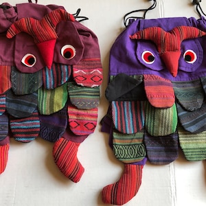 Puede incluir: Dos bolsas de cordón con forma de búho de colores con tejido de retazos rojo, morado, verde y negro. Las bolsas tienen picos rojos y ojos blancos.