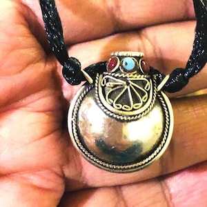 May include: A silver pendant necklace with a round, ornate design and a small, colorful stone inlay. The pendant is attached to a black cord.