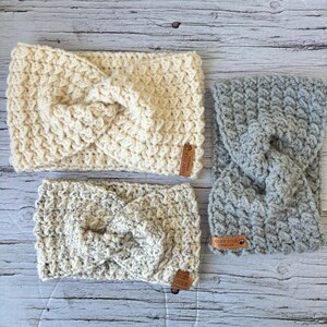 Op de afbeelding: Drie gebreide hoofdbanden in verschillende kleuren en patronen. De hoofdbanden zijn gemaakt met een dik garen en hebben een geknoopt ontwerp. De hoofdbanden zijn gelabeld met "Cozy Coils" en zijn een geweldige accessoire voor elke outfit.