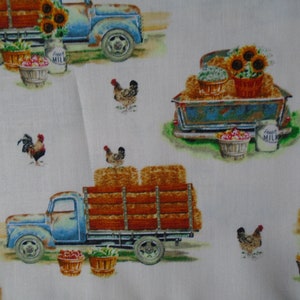 May include: A white fabric with a repeating pattern of blue vintage trucks carrying hay bales, sunflowers, and baskets of produce. The trucks have a 'Fresh Milk' label on the side. There are also chickens and roosters in the pattern.