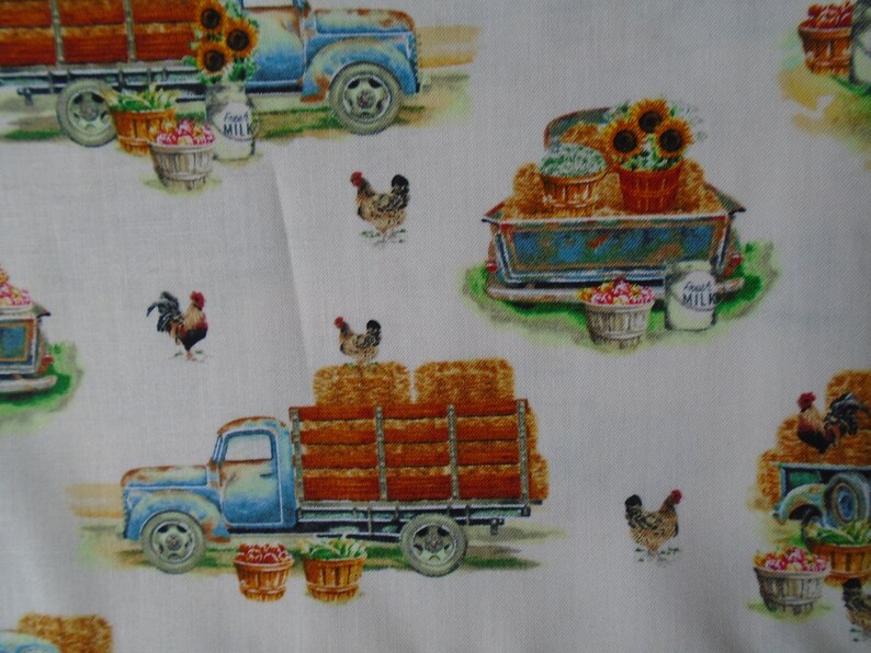 May include: A white fabric with a repeating pattern of blue vintage trucks carrying hay bales, sunflowers, and baskets of produce. The trucks have a 'Fresh Milk' label on the side. There are also chickens and roosters in the pattern.