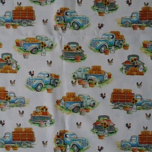 May include: A white fabric with a repeating pattern of blue vintage pickup trucks carrying hay bales, produce, and sunflowers. The trucks are surrounded by chickens and baskets of produce.