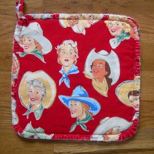 May include: Red fabric pot holder with a white border and a pattern of women wearing cowboy hats. The women are depicted in a vintage style with colorful clothing and accessories.