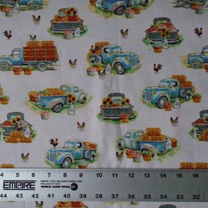 May include: A white fabric with a repeating pattern of blue pickup trucks carrying hay bales, sunflowers, and baskets of produce. The trucks are on a green grassy field with chickens and a ruler in the bottom of the image.