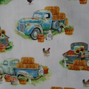 May include: A white fabric with a repeating pattern of blue vintage trucks, hay bales, sunflowers, chickens, and milk jugs. The trucks are carrying baskets of fruit and vegetables. The text "Good Milk" is printed on the milk jugs.