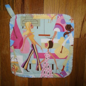 May include: A blue and white pot holder with a design of three women in colorful dresses and sunglasses. The women are walking and shopping.