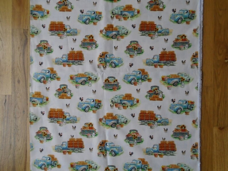 May include: White fabric with a repeating pattern of blue pickup trucks carrying hay bales. The trucks are surrounded by sunflowers, chickens, and baskets of produce.