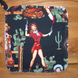 May include: A black and white pot holder with a fringed edge. The design features a woman in a red and white shirt and black shorts holding two pistols. The background includes cacti, a saddle, and a guitar.