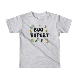 May include: A light gray t-shirt with a black circle design featuring the text "BUG EXPERT" surrounded by various cartoon bugs in shades of green, yellow, and brown.