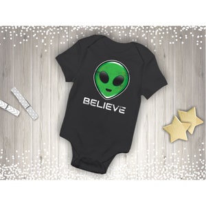 May include: Black baby onesie with a green alien face graphic and the word "BELIEVE" in white text.