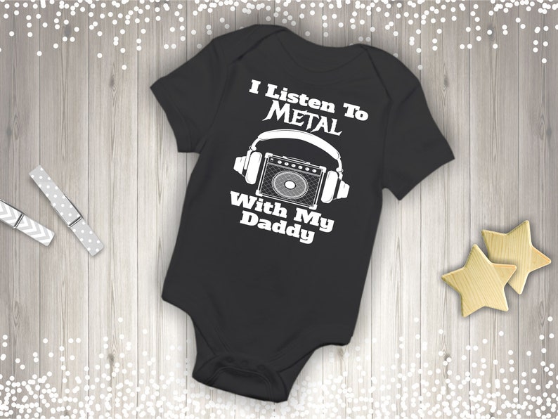 May include: Black baby onesie with white text that reads "I Listen To Metal With My Daddy". The onesie has a graphic of a microphone and headphones.
