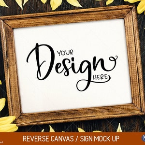 May include: A wooden frame with a white canvas insert. The canvas has the text "Your Design Here" written in black cursive. The frame is surrounded by yellow sunflower petals on a brown wooden background.