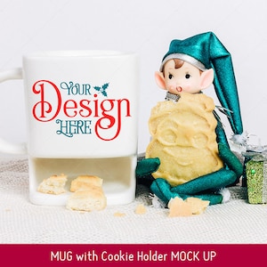 Puede incluir: Taza de cer&aacute;mica blanca con un soporte para galletas, con el texto "Your Design Here" en rojo y verde. Una mu&ntilde;eca de elfo verde sostiene una galleta y se sienta junto a la taza sobre una superficie blanca.