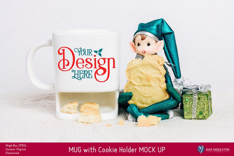 Puede incluir: Taza de cer&aacute;mica blanca con un soporte para galletas, con el texto "Your Design Here" en rojo y verde. Una mu&ntilde;eca de elfo verde sostiene una galleta y se sienta junto a la taza sobre una superficie blanca.
