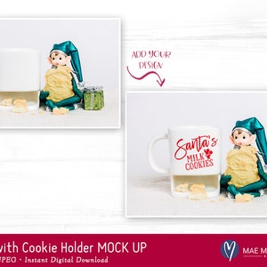 Puede incluir: Taza de cer&aacute;mica blanca con un soporte para galletas, con el texto "Santa's Milk & Cookies" en rojo. Un peque&ntilde;o mu&ntilde;eco de elfo sostiene una galleta y est&aacute; sentado junto a la taza.