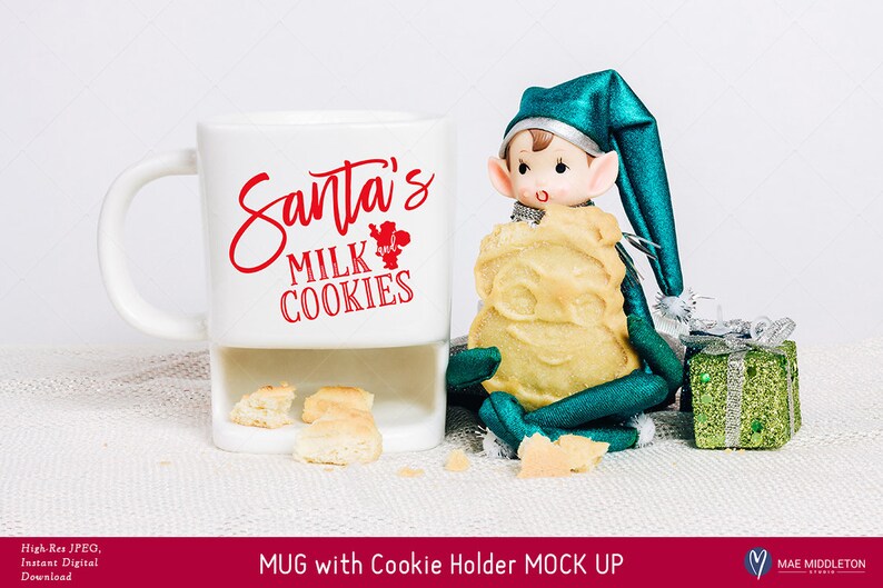 Puede incluir: Taza de cer&aacute;mica blanca con un soporte para galletas. La taza tiene texto rojo que dice "Santa's Milk and Cookies". Un mu&ntilde;eco de duende verde est&aacute; sosteniendo una galleta y sentado junto a la taza.