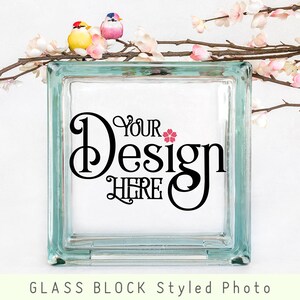 May include: A clear glass block with the text "Your Design Here" in black script font. The glass block is sitting on a white surface with a branch of pink blossoms and two small birds.