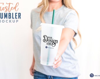 May include: A frosted clear plastic tumbler with a green straw. The tumbler has a white lid and the text "Your Design Here" printed on the side.