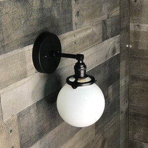 May include: Black wall sconce with a white frosted glass globe shade. The sconce has a simple design with a metal arm and a round base.