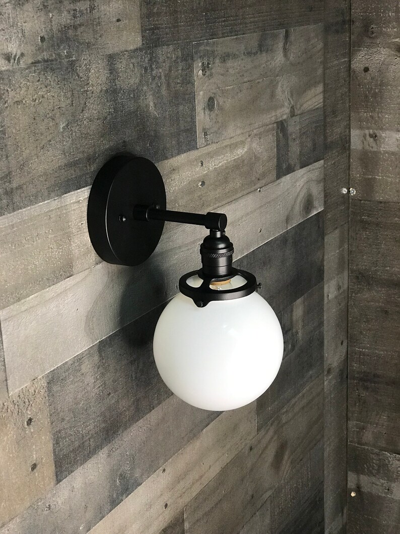 May include: Black wall sconce with a white frosted glass globe shade. The sconce has a simple design with a metal arm and a round base.