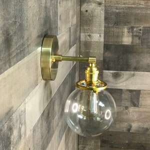 May include: A gold wall sconce with a clear glass globe shade. The sconce has a simple design and is perfect for adding a touch of modern style to any room.