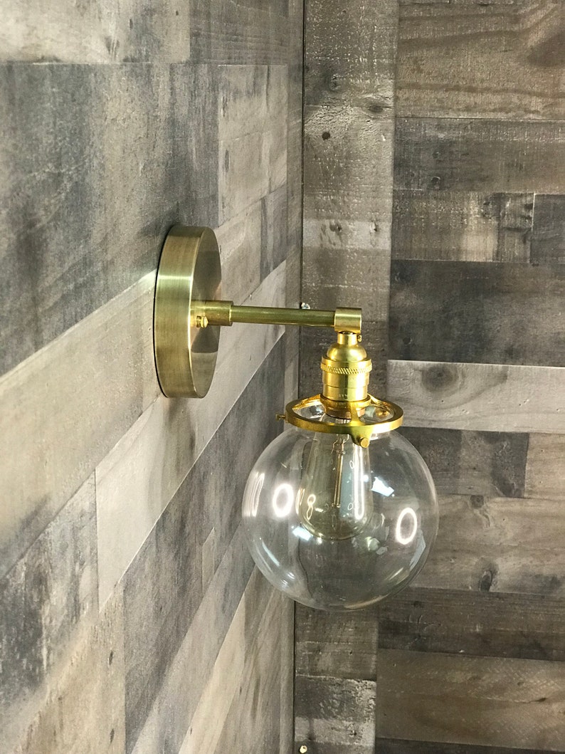 May include: A gold wall sconce with a clear glass globe shade. The sconce has a simple design and is perfect for adding a touch of modern style to any room.